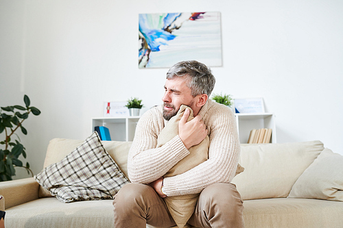 Sad desperate middle-aged bearded man in cardigan sitting on sofa and crying while dealing with personal issues at therapy in modern psychlogists office