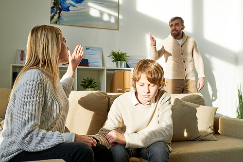 Serious young mother holding hand of son and protecting him while yelling at husband at home