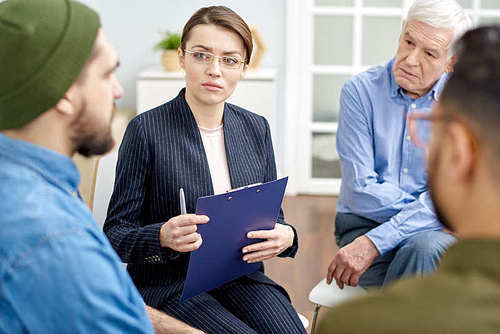 Highly professional psychologist in formalwear working with depressed patient while conducting group therapy session at cozy office