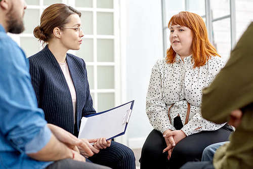 Highly professional young psychologist listening to her obese patient suffering from eating disorder with concentration while conducting group therapy session at cozy office