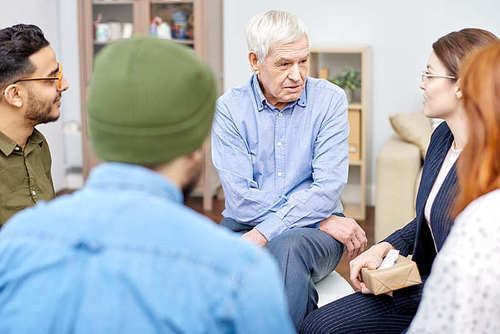 Support group of different age having psychological therapy: they sitting in circle and sharing their problems with highly professional psychologist and other patients