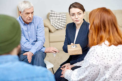 Friendly young psychiatrist passing paper tissue box to obese patient while conducting group therapy session at cozy office