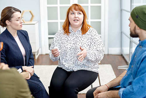Profile view of pretty young psychologist listening to her obese patient suffering from eating disorder with concentration while conducting group therapy session