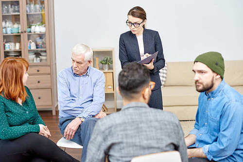 Group of patients training their social skills while sitting in circle and participating in therapy session, highly professional psychologist keeping eye on them