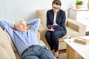 Portrait shot of senior man lying on cozy sofa with hands on nape while discussing faced problem with highly professional psychiatrist during productive therapy