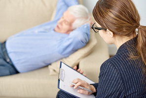 Senior patient lying on cozy sofa with hands on nape and sharing his problems with highly professional psychologist while having therapy session