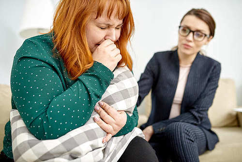 Depressed red-haired woman expressing her feeling while having consultation with highly professional psychiatrist, interior of cozy office on background