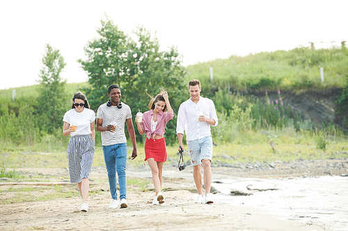 Group of friends enjoying leisure time on fresh air outdoors. They walking with drinks in non-urban area
