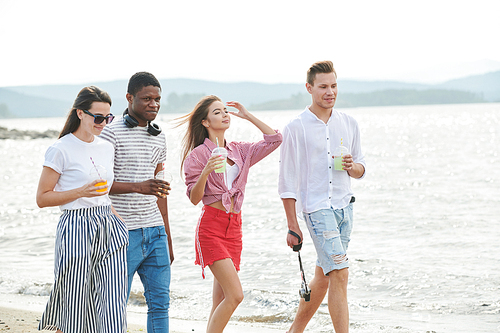 Young people drinking juice, walking along the coast and enjoying their summer vacation