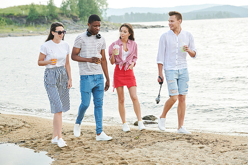 Group of teenagers walking on the beach and drinking lemonade