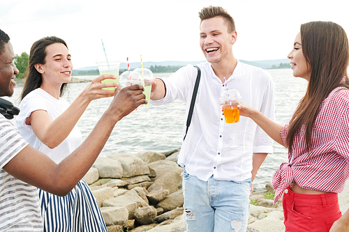 Happy young people drinking cocktails and toasting while standing against the lake