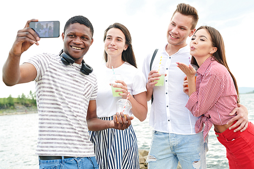 Happy young people standing and making selfie portrait on mobile phone during summer vacation