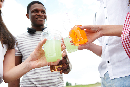 Close-up of teenagers holding plastic glasses with cocktails and toasting, they celebrating something