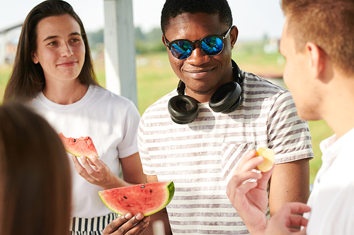 African young man in sunglasses eating watermelon with his friends during a picnic