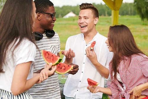 Cheerful young friends eating watermelon having fun together outdoors