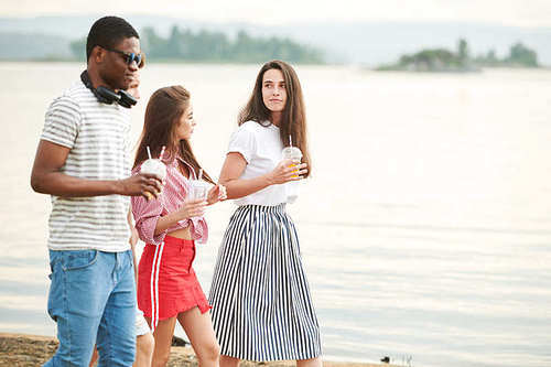 Young people with cold drinks spending their time near the lake outdoors