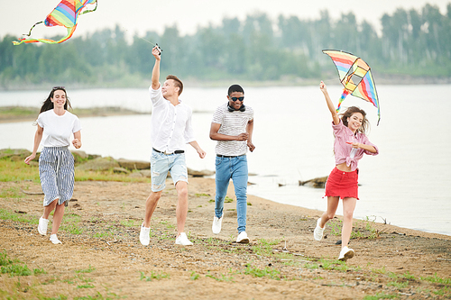 Group of happy teenagers playing with flying kites outdoors, they running on the beach