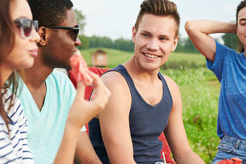 Young smiling man sitting on picnic on the nature together with friends