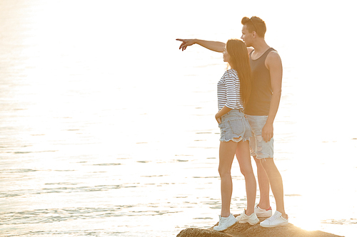 Romantic young couple standing on the rock and looking at horizon together