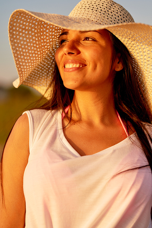 Happy smiling dreamy beautiful young Hispanic woman in sun hat looking into distance outdoors while being on summer vacation