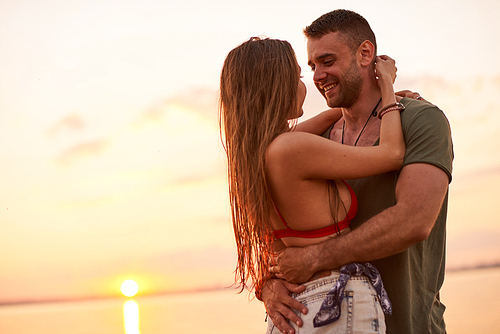 Cheerful romantic beautiful young couple talking and cuddling while enjoying at sunset sea