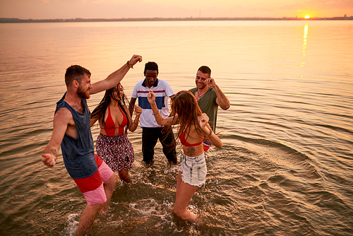 Cheerful excited wet young multiethnic friends having and dancing in water during sea party