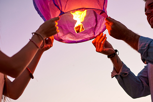 Close-up of young couple holding sky paper lantern with burning candle inside and preparing to launch it into sky