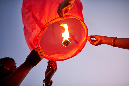 Below view of couple making wish and preparing to launch flying lantern to sky as symbol of eternal love outdoors