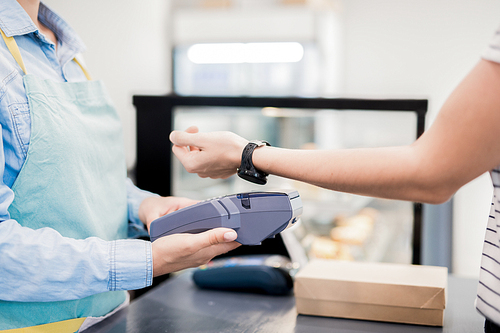 Close up of unrecognizable woman paying via smart watch in local bakery, copy space