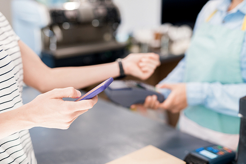 Close up of unrecognizable woman paying via NFC smartphone in local shop, copy space