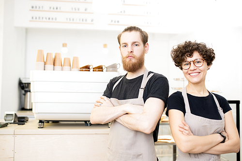 Positive confident young team of coffee shop staff standing at espresso machine and  while crossing arms on chest