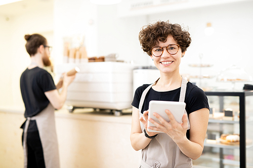 Smiling pretty waitress in apron and glasses standing in coffee shop and , she using tablet to take order