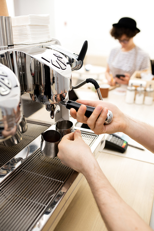 Close-up of unrecognizable barista making espresso using coffee machine, man attaching portafilter and holding metal jugs for coffee