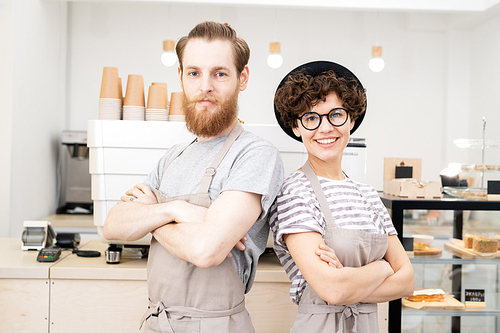 Positive confident hipster couple of baristas in aprons standing against espresso machine and 