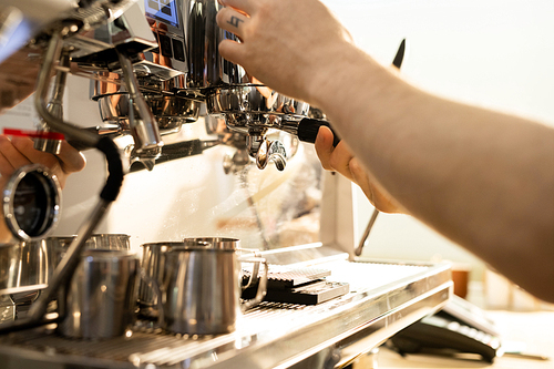 Close-up of unrecognizable male barista brewing coffee using espresso machine: he adjusting portafilter