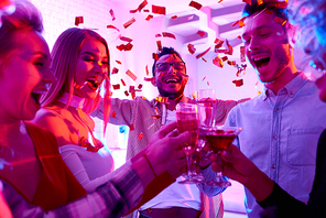 Group of happy friends enjoying holiday celebration at private house party raising glasses  and toasting under bursts of confetti