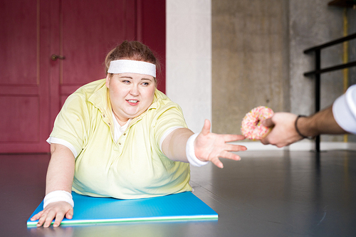 Portrait of straining fat woman working out in fitness club and reaching for donut, copy space