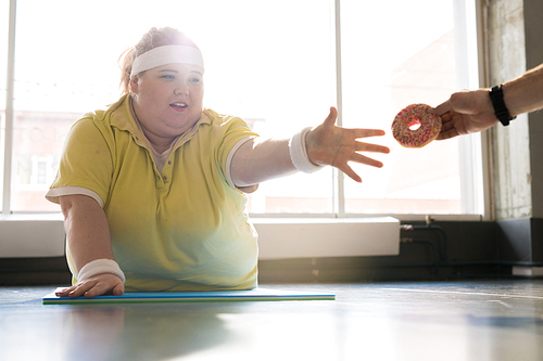 Portrait of young  fat woman working out in fitness club and reaching for donut, copy space