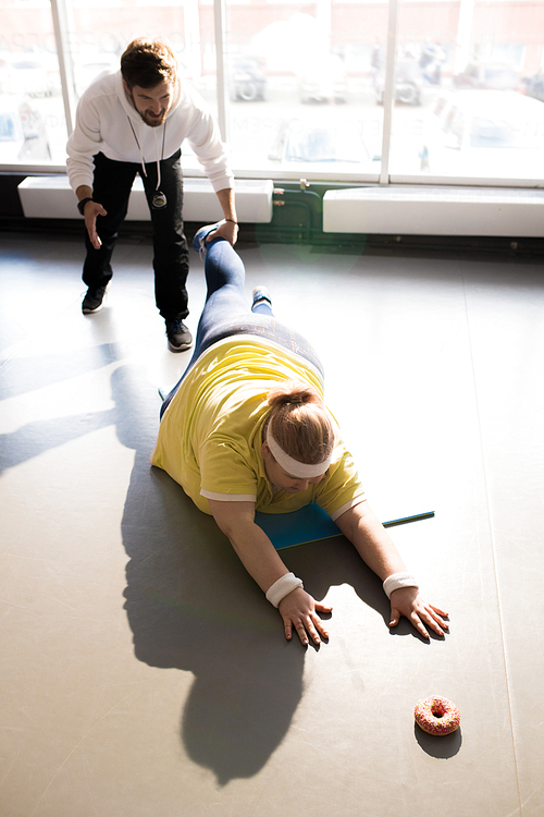 Full length high angle portrait of obese young woman working out with personal coach in fitness club