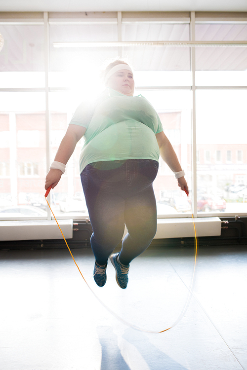 Full length portrait of obese young woman jumping rope during workout in sunlight