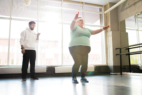 Full length portrait of fat woman exercising during workout with fitness coach, copy space