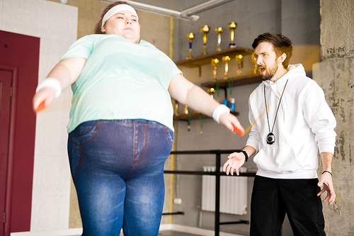 Waist up portrait of angry coach shouting at  fat woman during training in fitness club, copy space