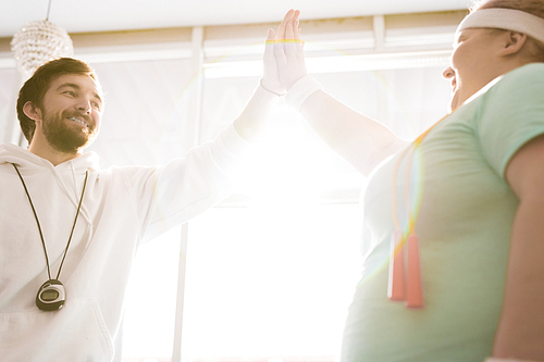 Portrait of smiling fitness coach high fiving with fat young woman during workout in sunlight