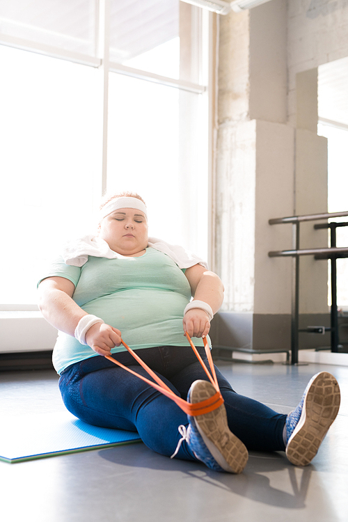 Full length portrait of young obese woman exercising with elastic band in fitness club, copy space