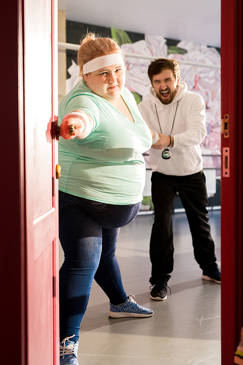 Full length portrait of fat woman trying to escape training in fitness club with coach struggling to hold her