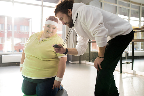 Portrait of happy obese woman looking at timer during weight loss workout in fitness club