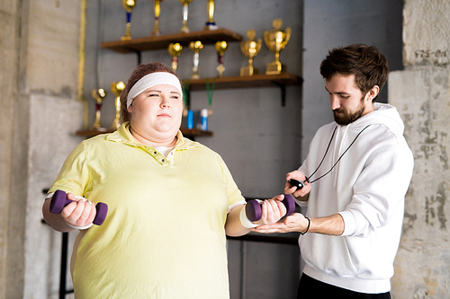 Waist up portrait of motivated overweight woman working out with dumbbells during weight loss training with fitness instructor