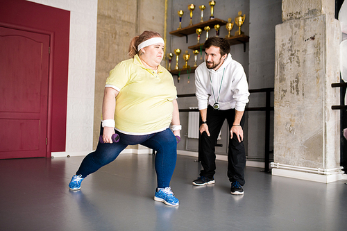 Full length portrait of motivated overweight woman working out during weight loss training with fitness instructor