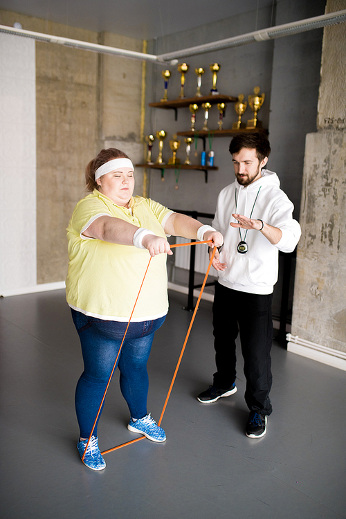 Full length portrait of obese young woman working out with personal fitness instructor in health club