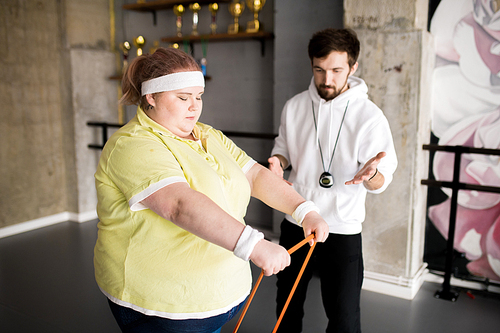 Waist up portrait of obese young woman working out with personal fitness instructor in health club, copy space